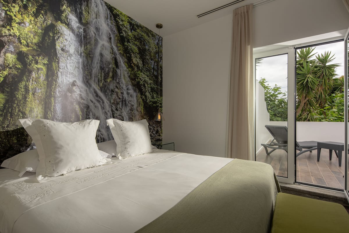 A hotel room with a large bed, a mural of a waterfall, and a balcony with outdoor furniture.