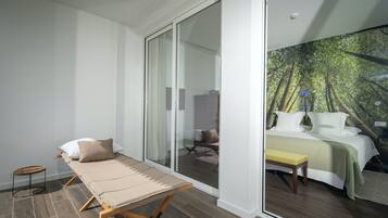 Une chambre à coucher comprenant un lit, un banc et une porte-fenêtre coulissante donnant sur une salle de bain.