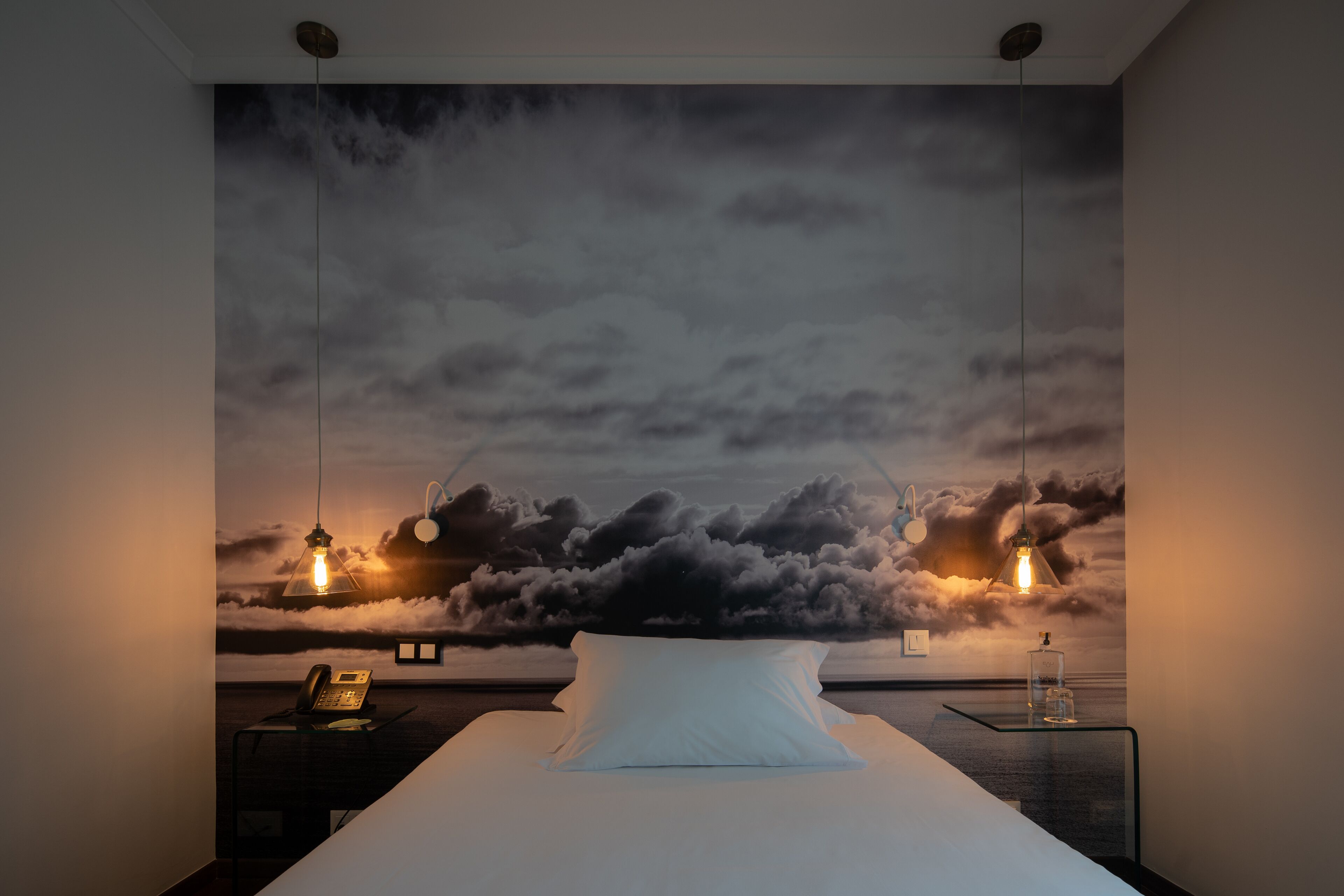 Ein Schlafzimmer mit einem Bett, einem Nachttisch, einer Lampe und einer Wandmalerei von Wolken.