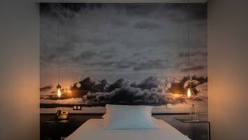Ein Schlafzimmer mit einem Bett, einem Nachttisch, einer Lampe und einer Wandmalerei von Wolken.