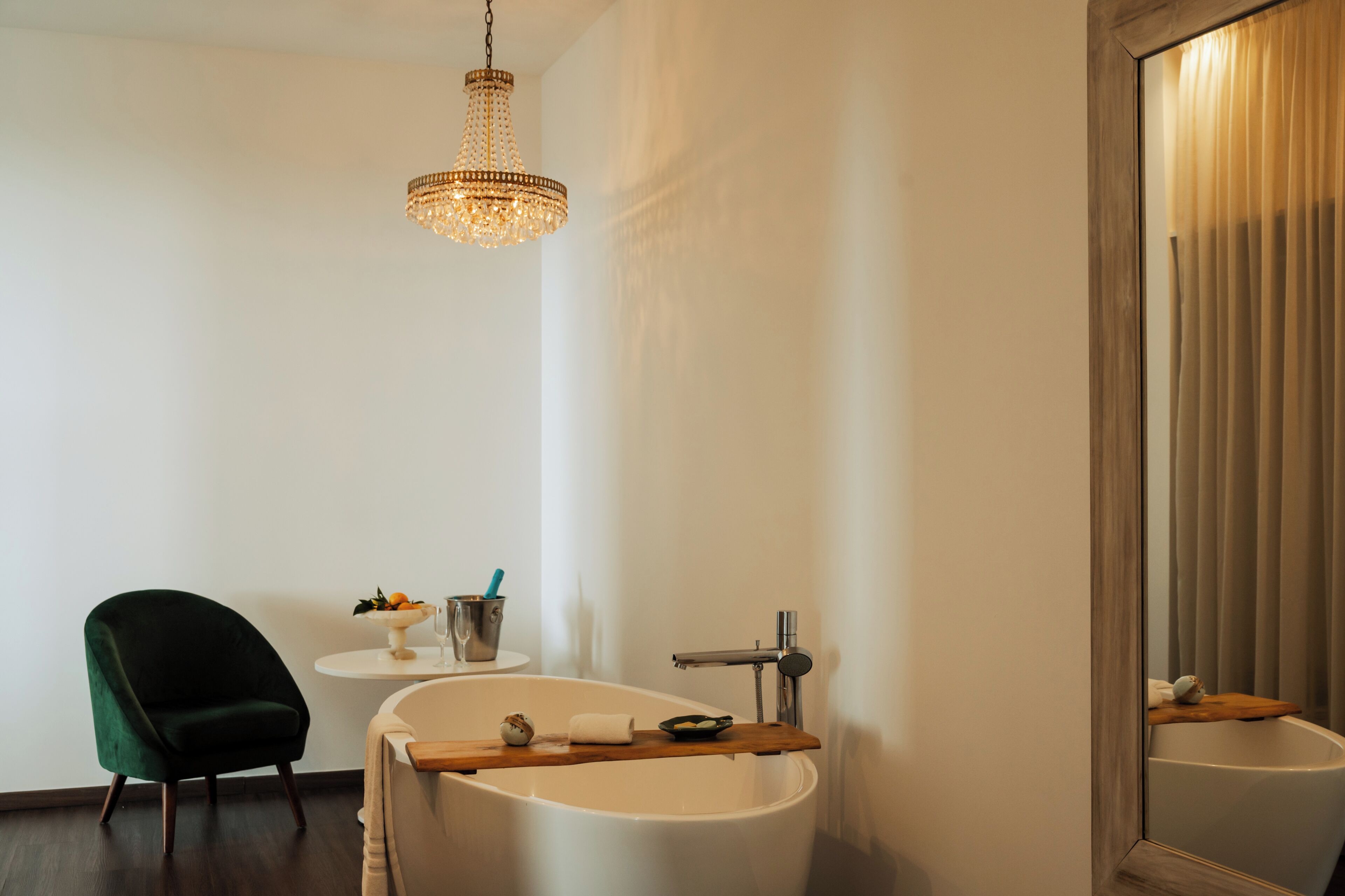 Une salle de bain moderne avec une baignoire sur pieds, un miroir rond, une chaise verte et un lustre.