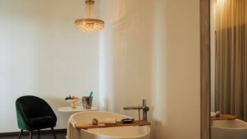 Une salle de bain moderne avec une baignoire sur pieds, un miroir rond, une chaise verte et un lustre.