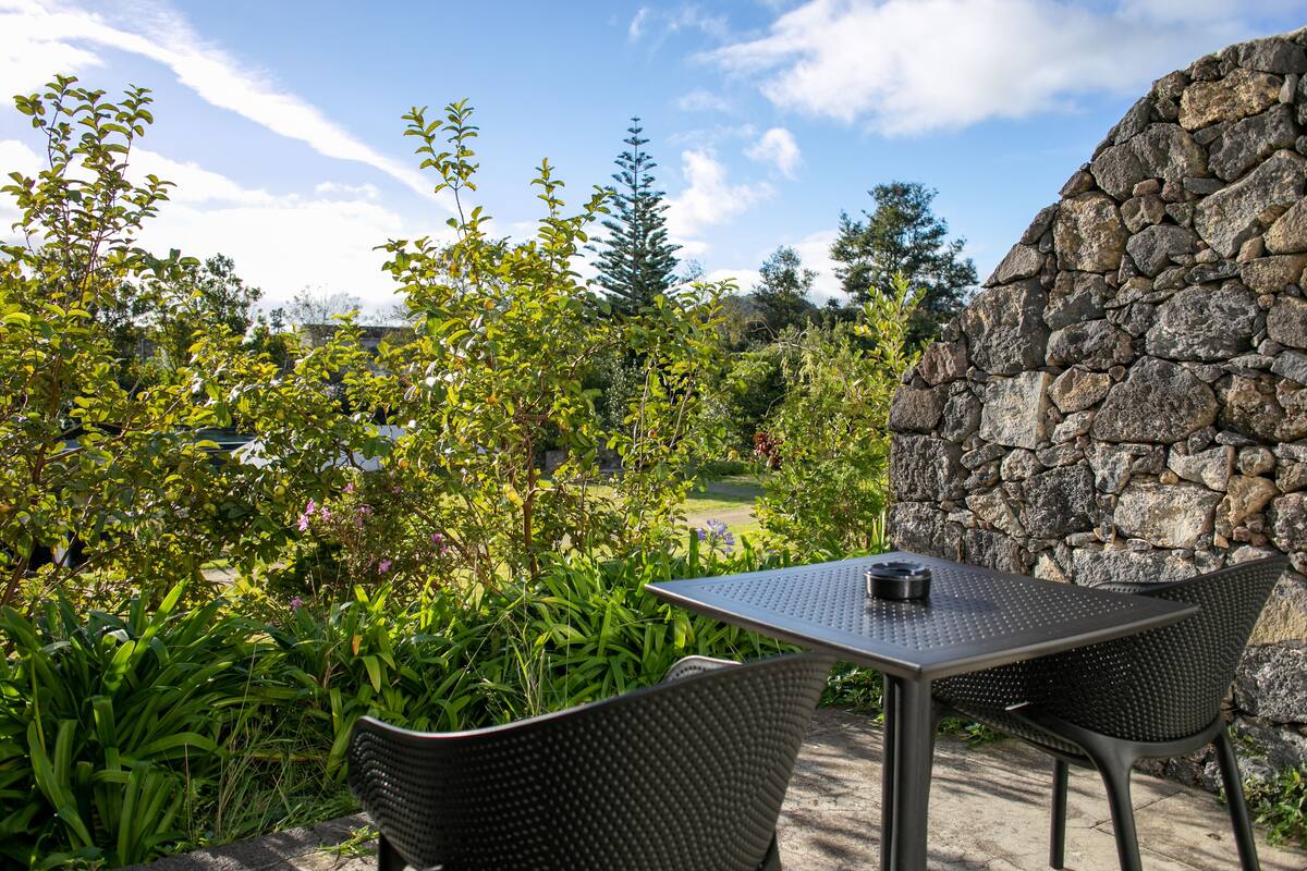An outdoor patio with a stone wall, two chairs, and a table.