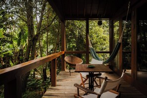 Une terrasse en bois avec un hamac, une chaise en osier et une table sur laquelle se trouve un saladier vert.