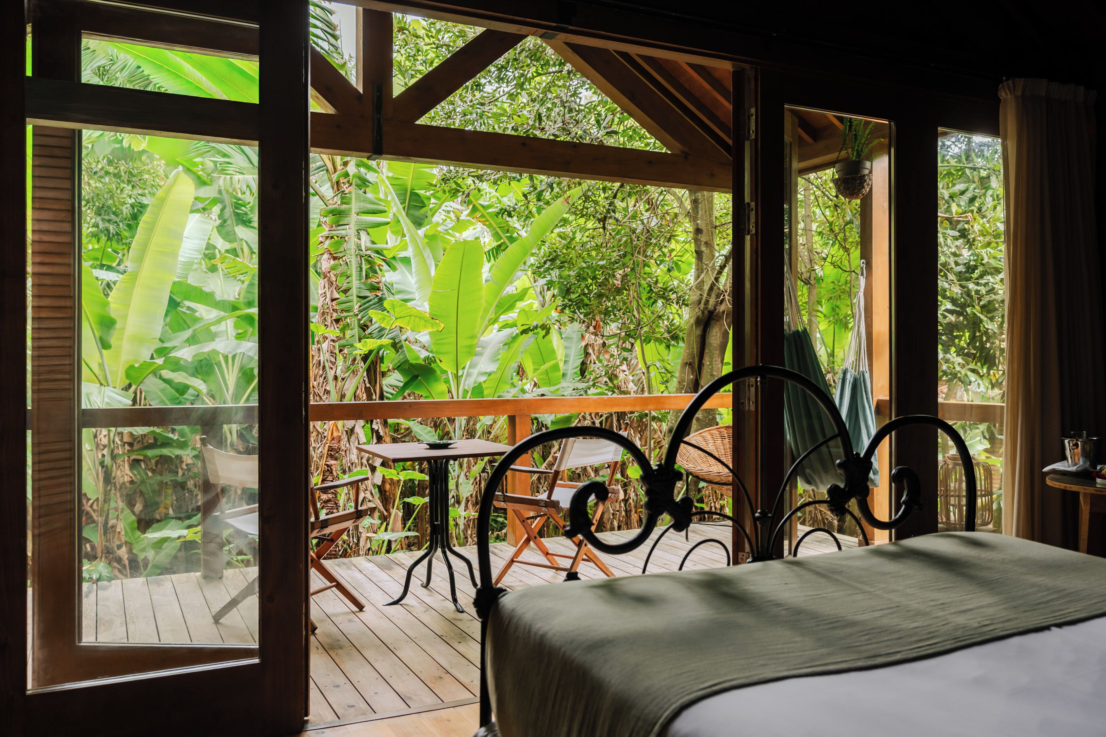 A room with a bed, a table, and chairs, with a view of lush greenery outside.