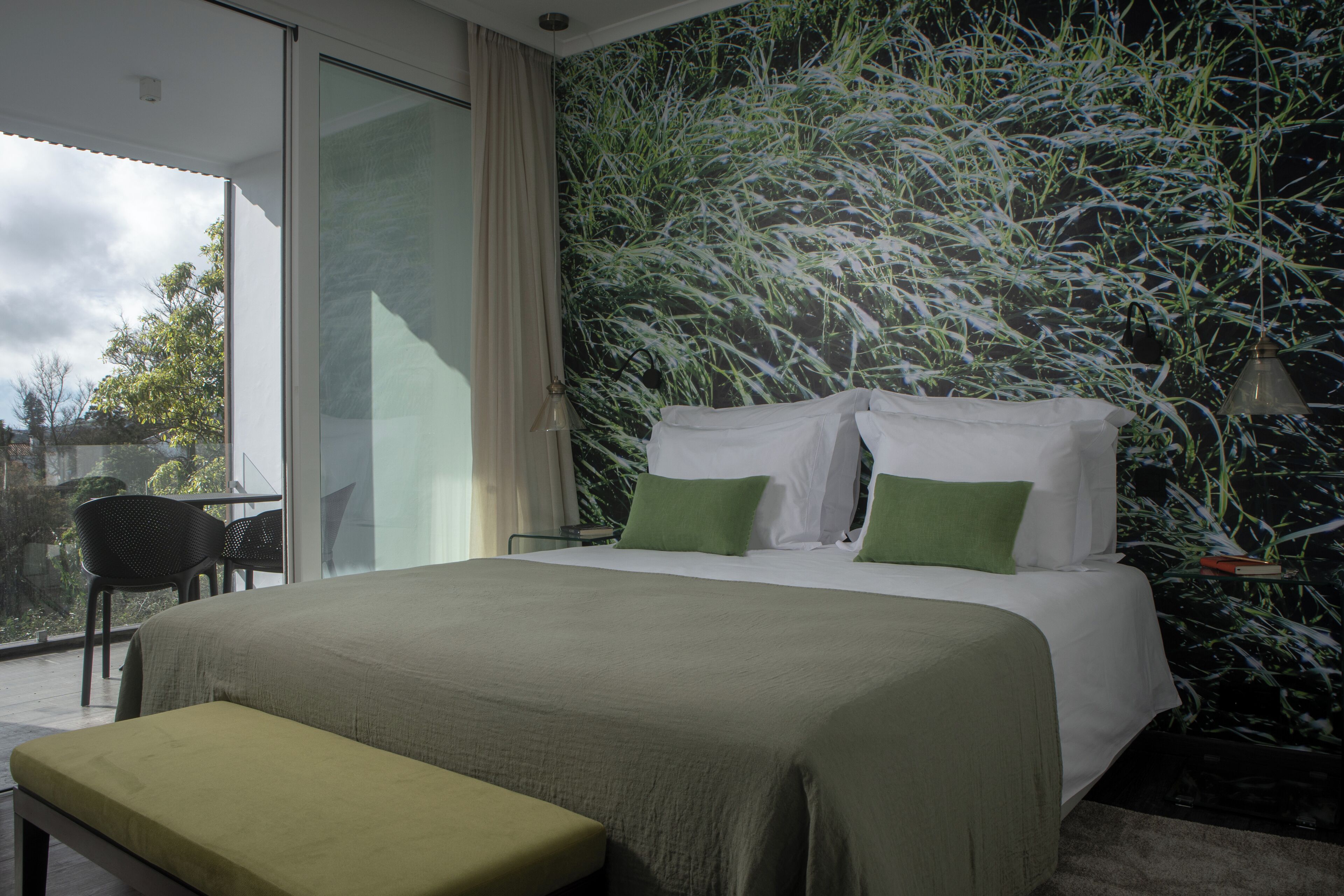 Quarto com uma cama grande, um banco, uma cadeira e vista para o exterior.