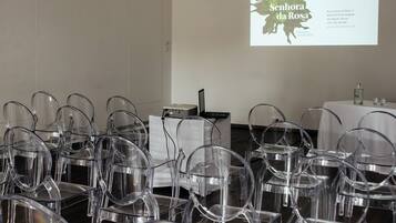 Una sala de conferencias con sillas de plástico transparente dispuestas en filas, una pantalla de proyección mostrando texto, y una mesa con una computadora portátil y una botella.
