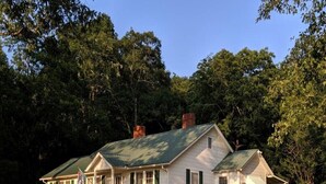 A white house with green shutters and a green roof, surrounded by trees.