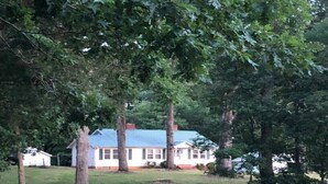 A gravel path leading to a white house with a blue roof, surrounded by trees.