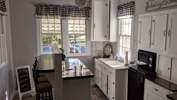 A kitchen with white cabinets, a central island, a ceiling fan, and a chalkboard sign.