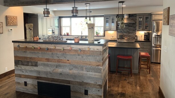 Une cuisine moderne dotée d’un îlot central, de poutres en bois, de luminaires suspendus et d’appareils électroménagers en acier inoxydable.