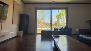 A spacious living room with a wooden floor, a large window, and a black leather sofa.