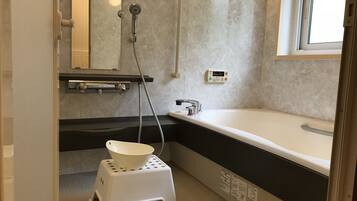 A bathroom with a bathtub, a small stool, a mirror, and a window.