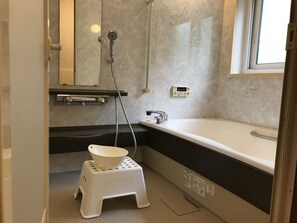 A bathroom with a bathtub, a small stool, a mirror, and a window.