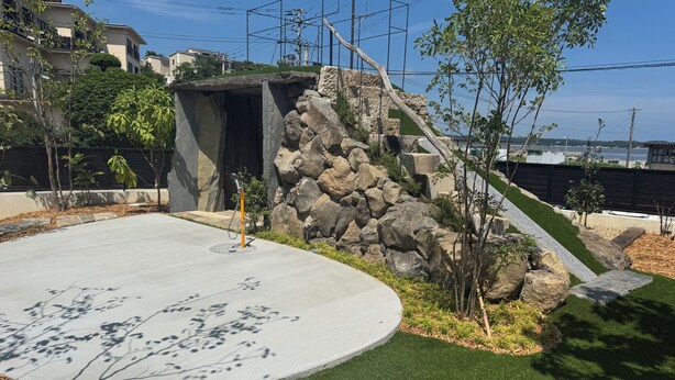 A landscaped area with a concrete path, green grass, and a stone structure.