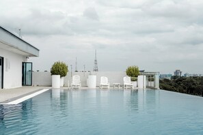 A rooftop infinity pool with white lounge chairs and potted plants, overlooking a cityscape with a prominent tower. - Regatta Stay Kozi Square Kuching (Kuching)
