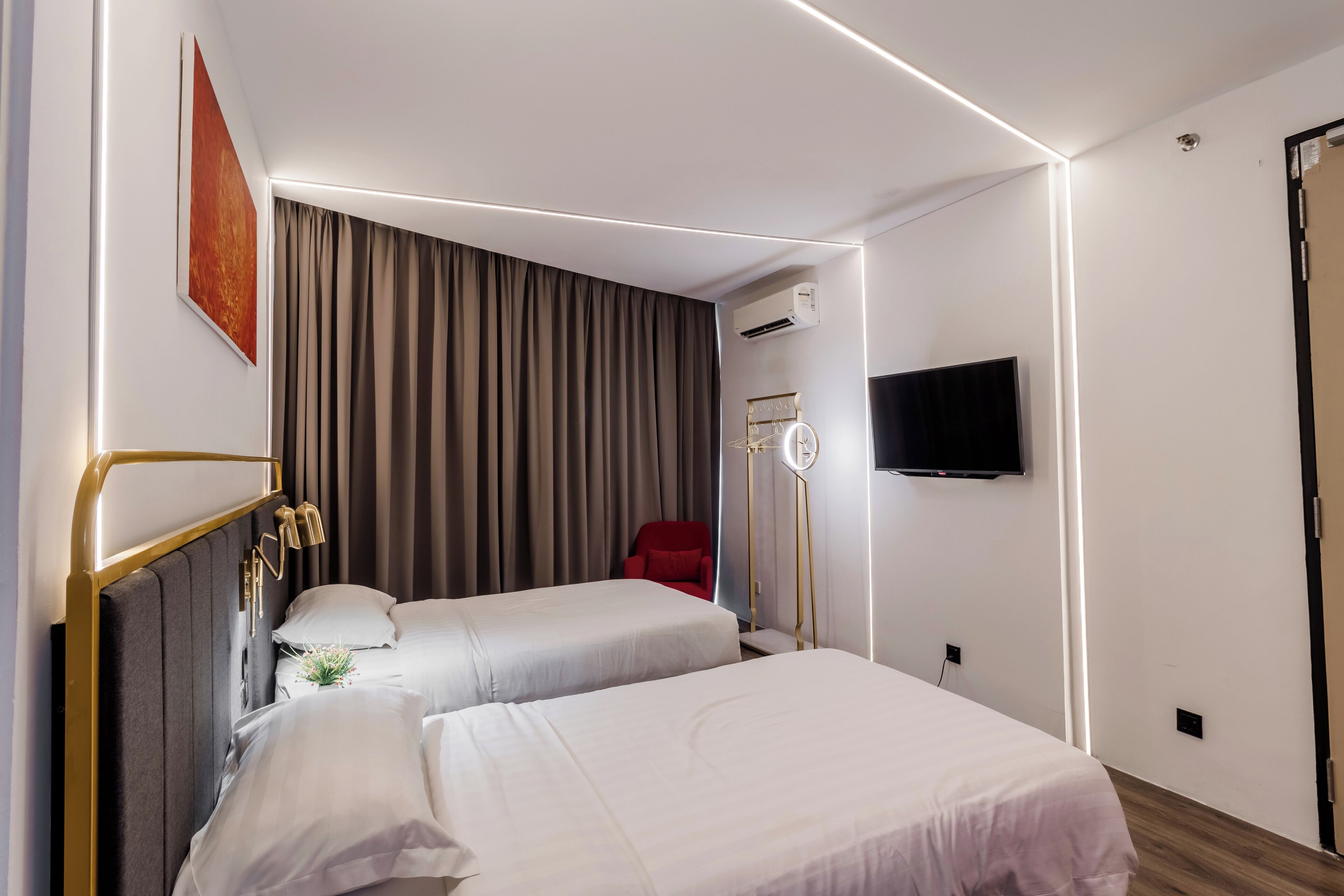 Een hotelkamer met twee bedden, een flatscreen televisie, een airconditioning en een rode stoel.