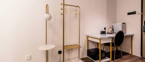 Una habitación moderna con un escritorio blanco, una lámpara de pie con marco dorado y una silla negra.