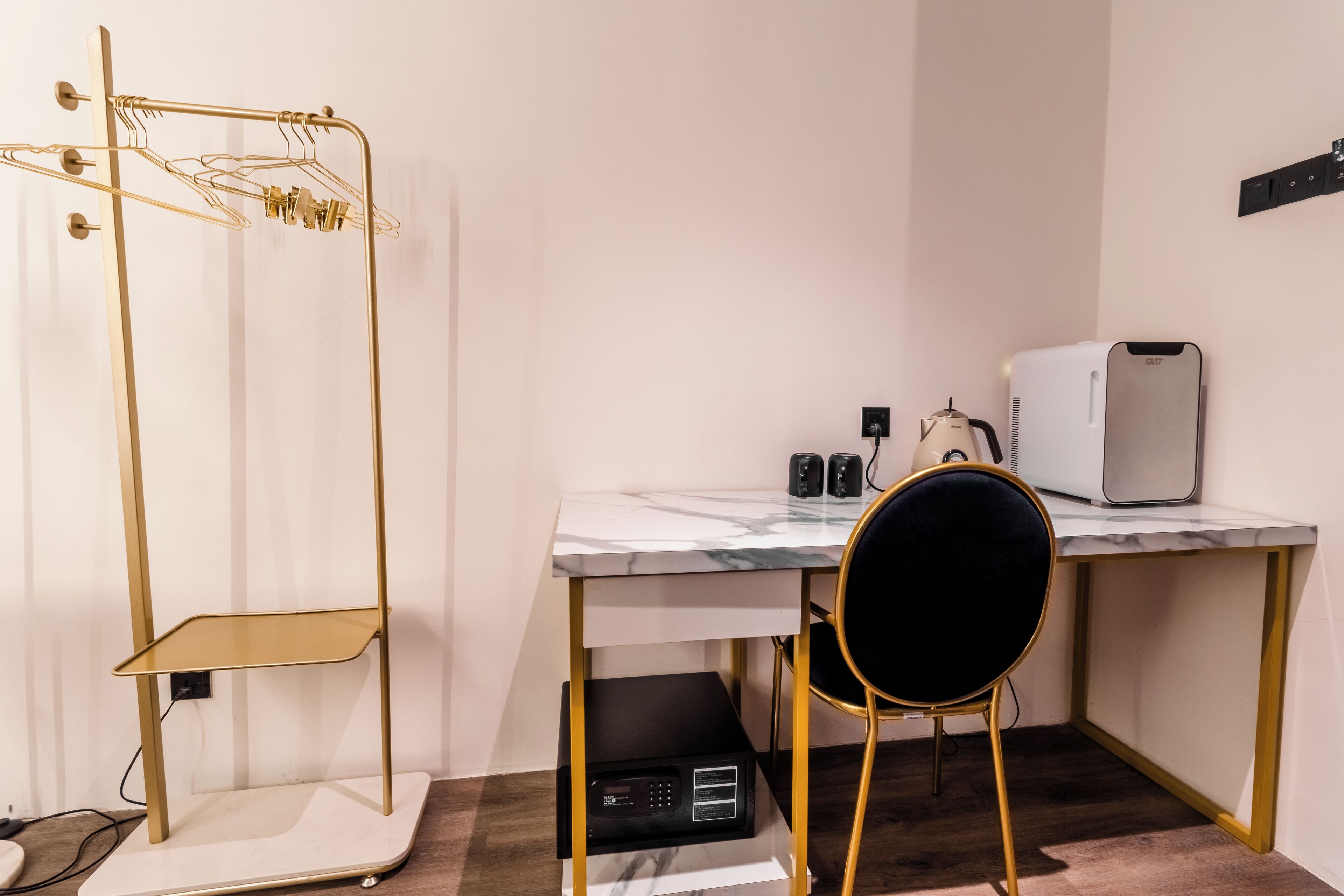 Una habitación compacta con escritorio, una silla, microondas, estante pequeño y perchero.