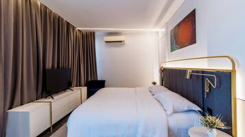 A modern hotel room with a large bed, a TV, a desk, and a small side table with a vase.
