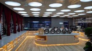 A modern restaurant with a central island, multiple seating areas, and a kitchen in the background. - Regatta Stay Kozi Square Kuching (Kuching)