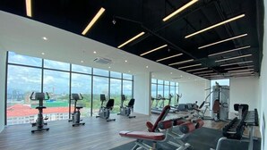A modern gym with various exercise equipment, large windows offering a view of the city, and a high ceiling with exposed beams. - Regatta Stay Kozi Square Kuching (Kuching)