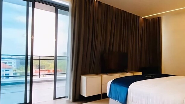A modern hotel room with a large bed, a flat-screen TV, a sliding glass door leading to a balcony, and a city view. - Regatta Stay Kozi Square Kuching (Kuching)