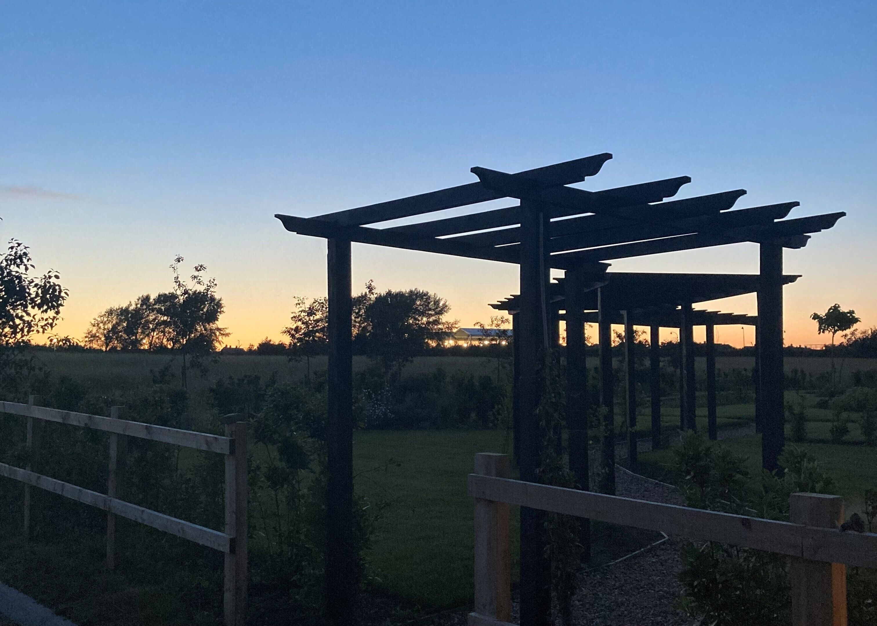 A pergola structure in a rural setting with a clear sky.