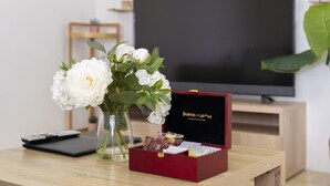 Una mesa de madera con un jarrón de flores blancas, una caja roja cerrada y un control remoto.