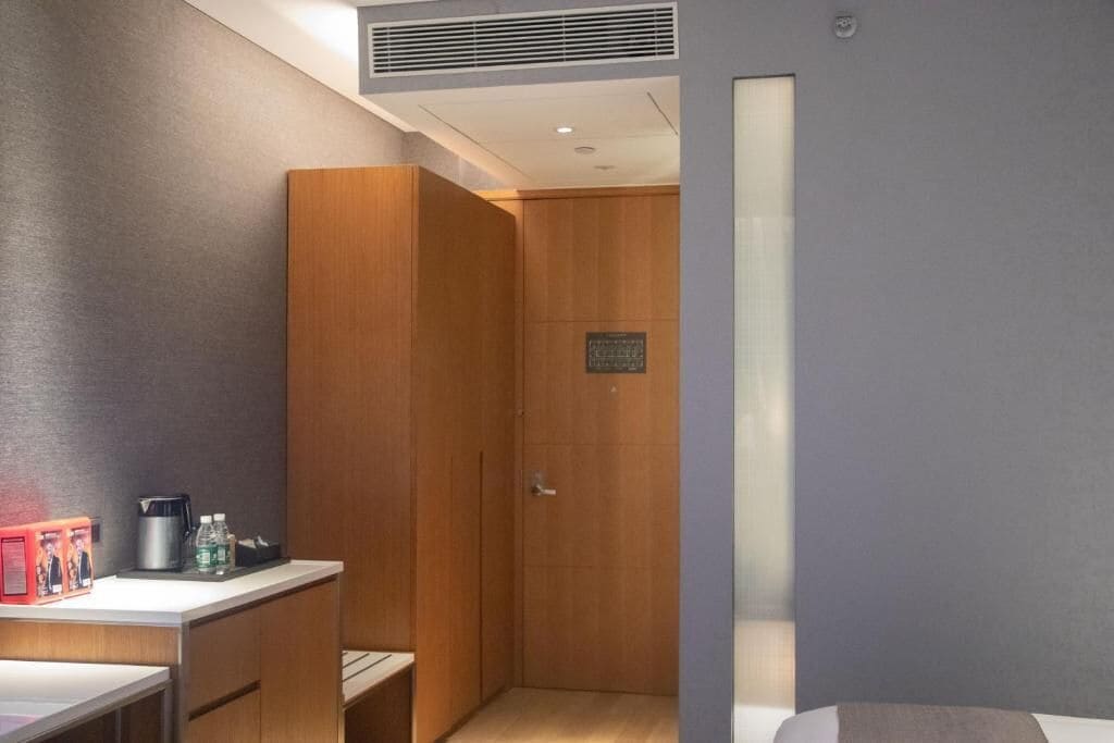 Ein modernes Hotelzimmer mit einem Holzschrank, einem kleinen Schreibtisch mit Kaffeemaschine und einem Bett.