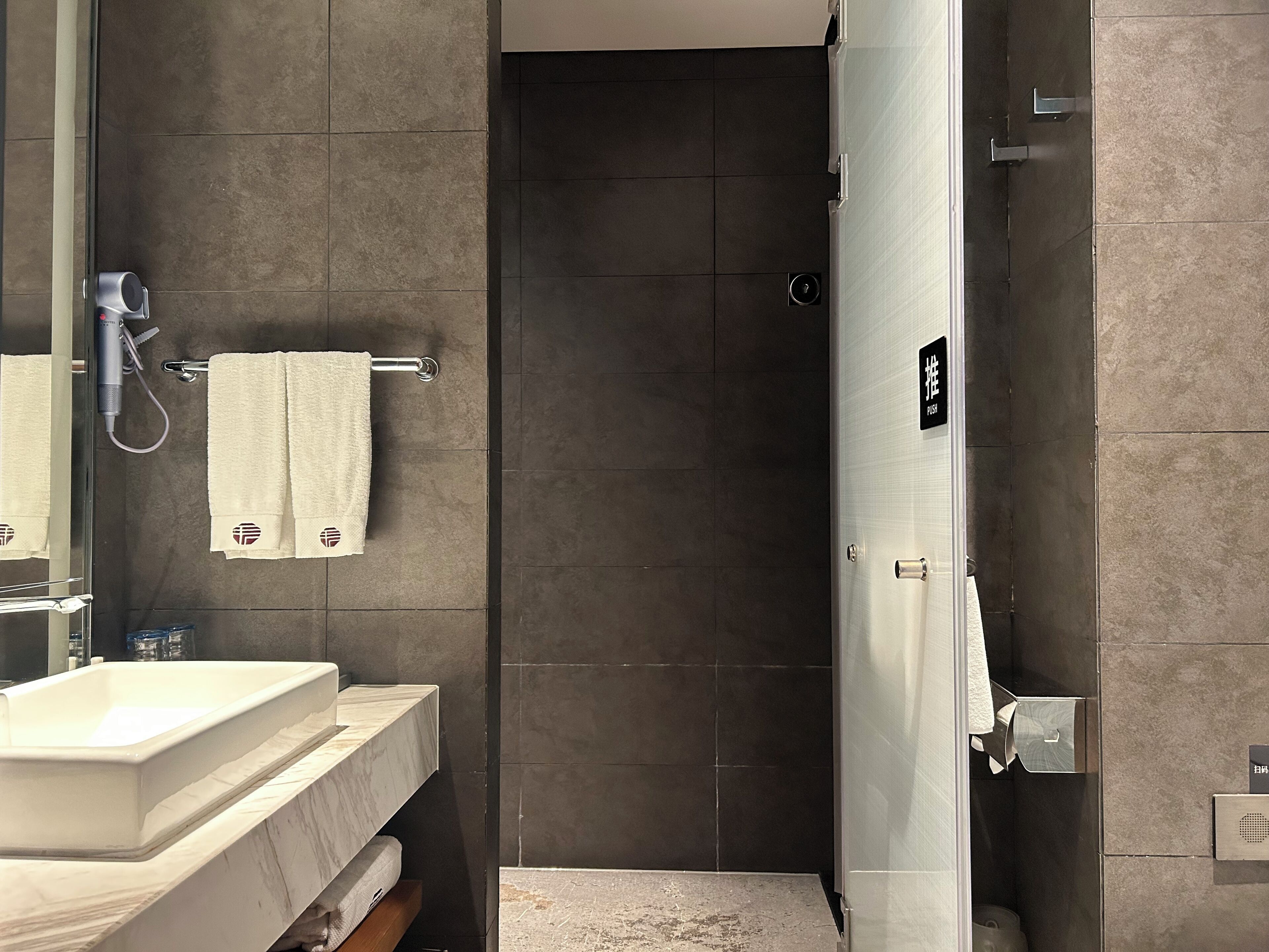 Ein modernes Badezimmer mit großem Spiegel, Waschbecken, Handtuchhalter und Duschbereich.