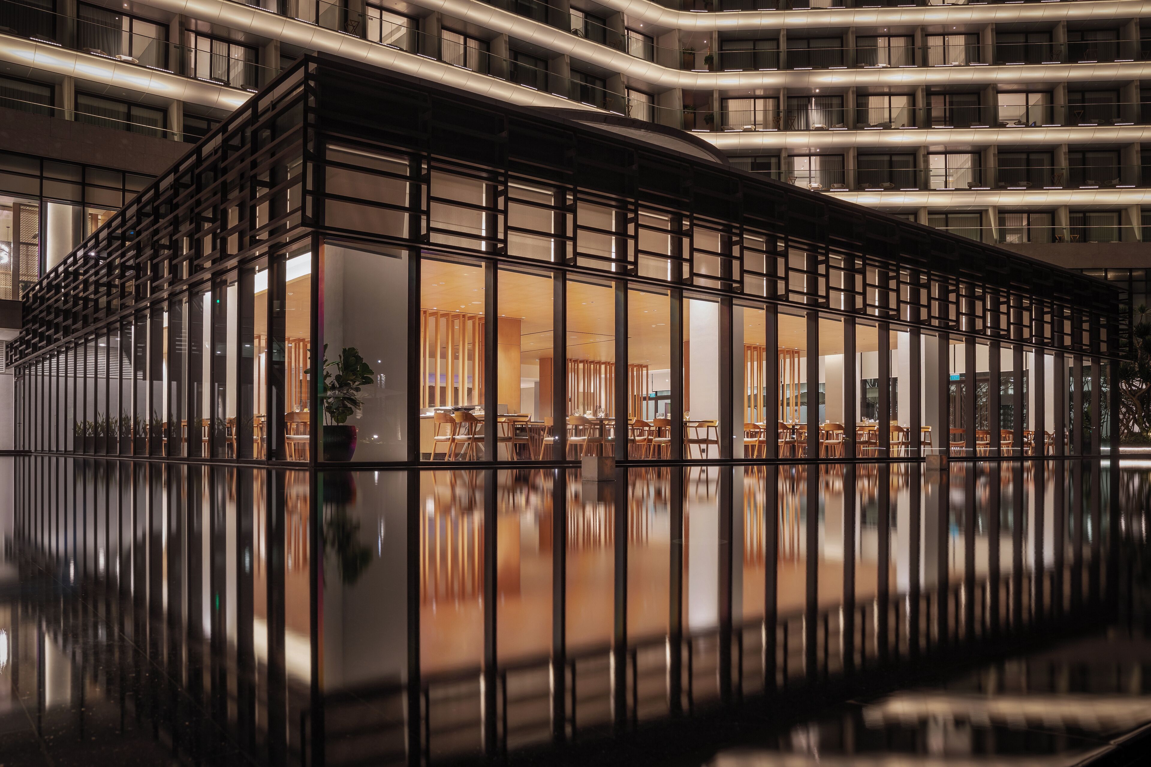 A modern hotel interior with a reflective floor, a central seating area, and a glass facade.