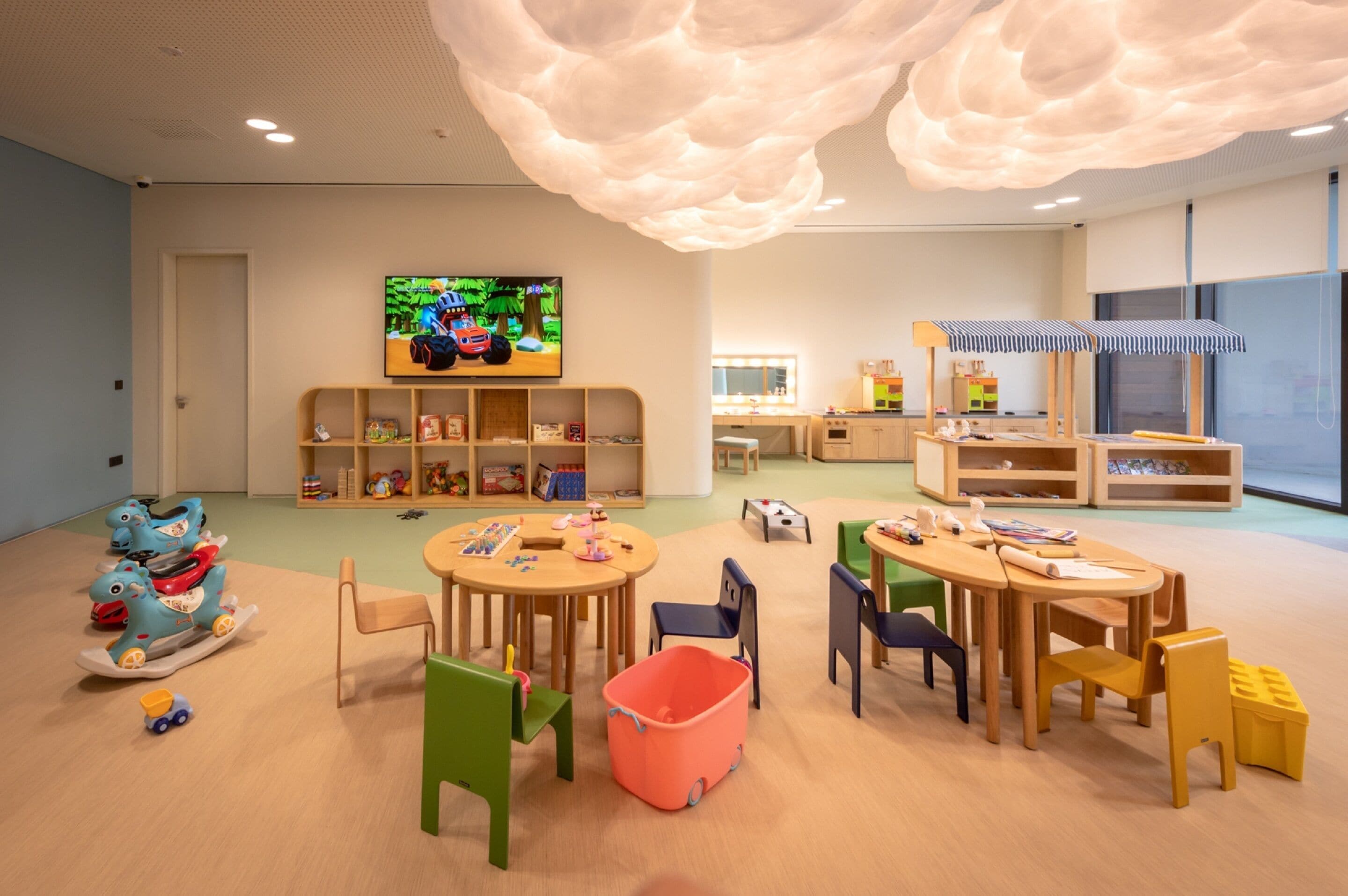 A children's playroom with a large TV, wooden shelves, and colorful toys.