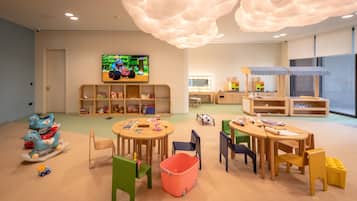 A children's playroom with a large TV, wooden shelves, and colorful toys.