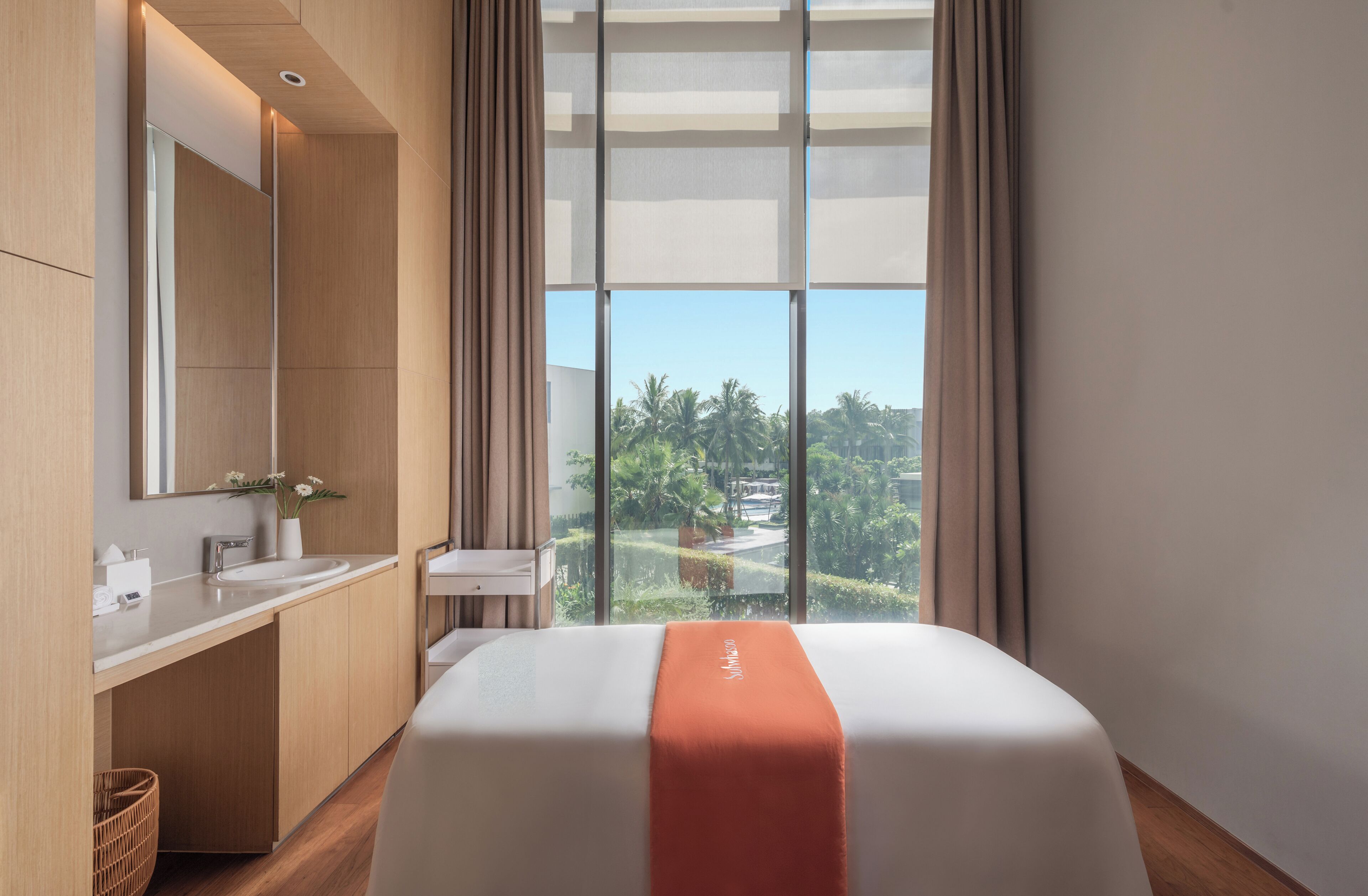 A hotel room with a large window, a bed, a bathroom with a sink, and a mirror.