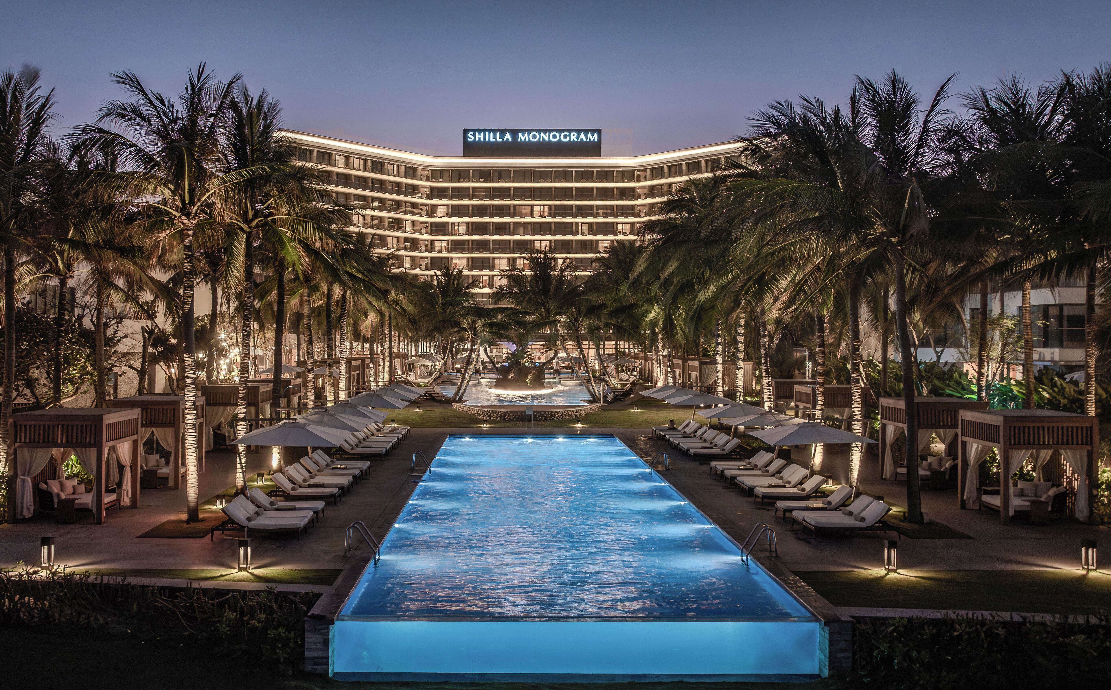 A hotel with a pool, sun loungers, and palm trees.