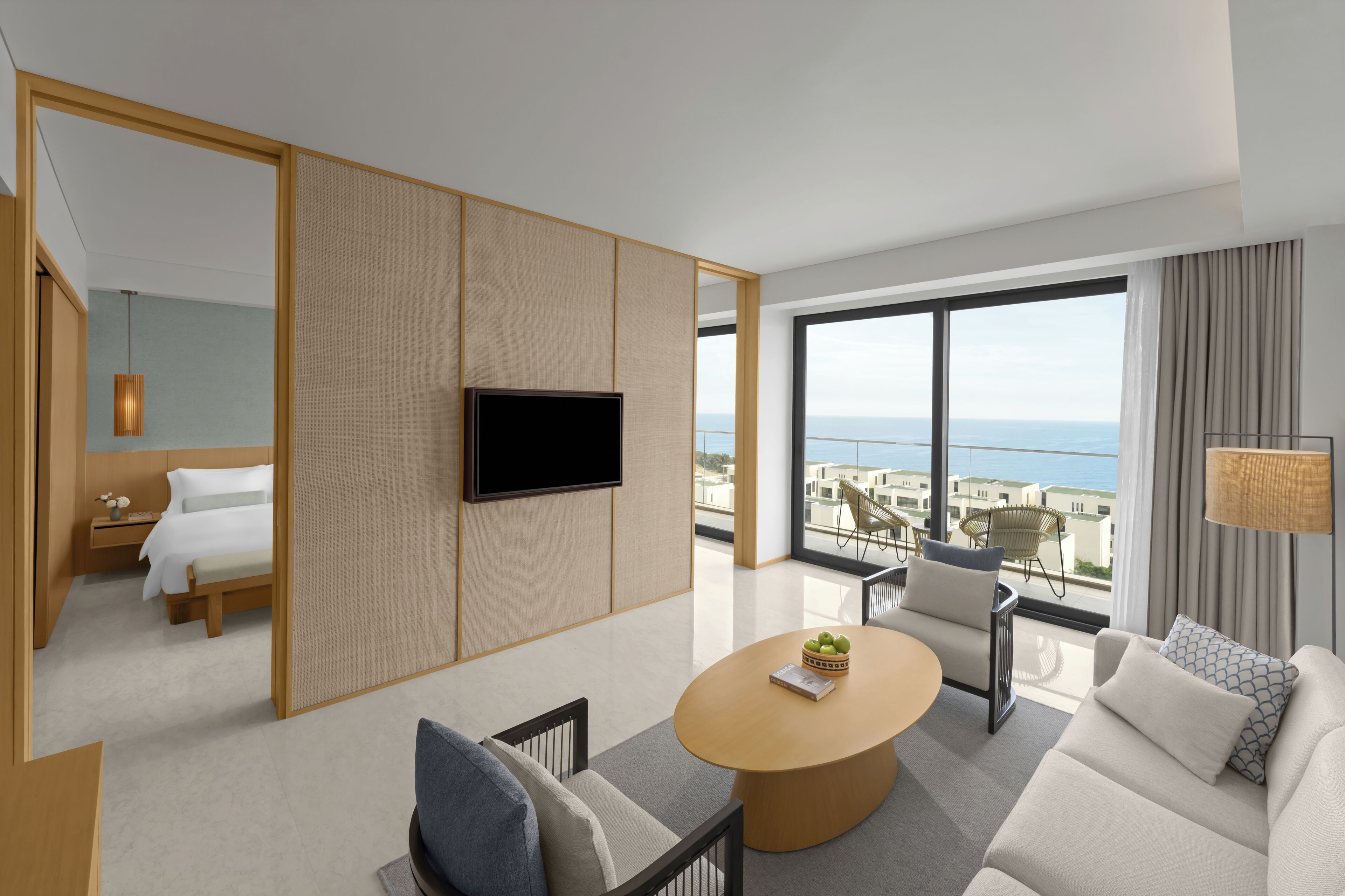 A modern hotel room with a large balcony, a flat-screen TV, a round wooden coffee table, a sofa, and a bed.