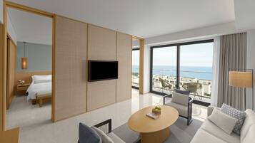 A modern hotel room with a large balcony, a flat-screen TV, a round wooden coffee table, a sofa, and a bed.