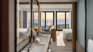 A modern hotel room with a large window, a bathroom with two sinks, a bed, and a seating area with a view of the ocean. - Shilla Monogram Danang (Da Nang)