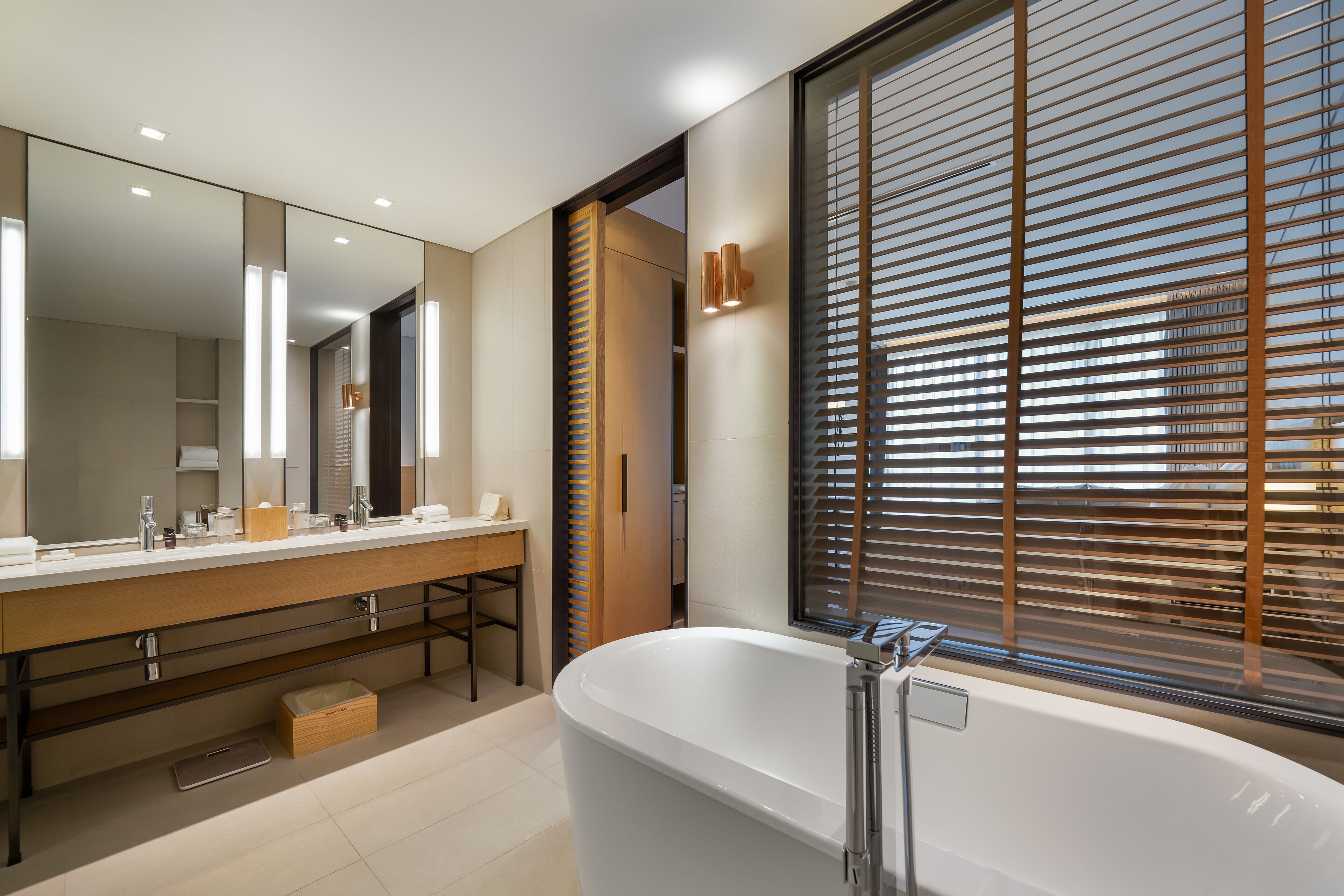 A modern bathroom with a large mirror, a bathtub, and a window with blinds.