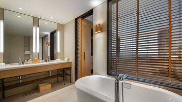 A modern bathroom with a large mirror, a bathtub, and a window with blinds.