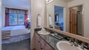 Une chambre d’hôtel avec un lit, un grand miroir, une coiffeuse avec un lavabo et une fenêtre avec des rideaux.