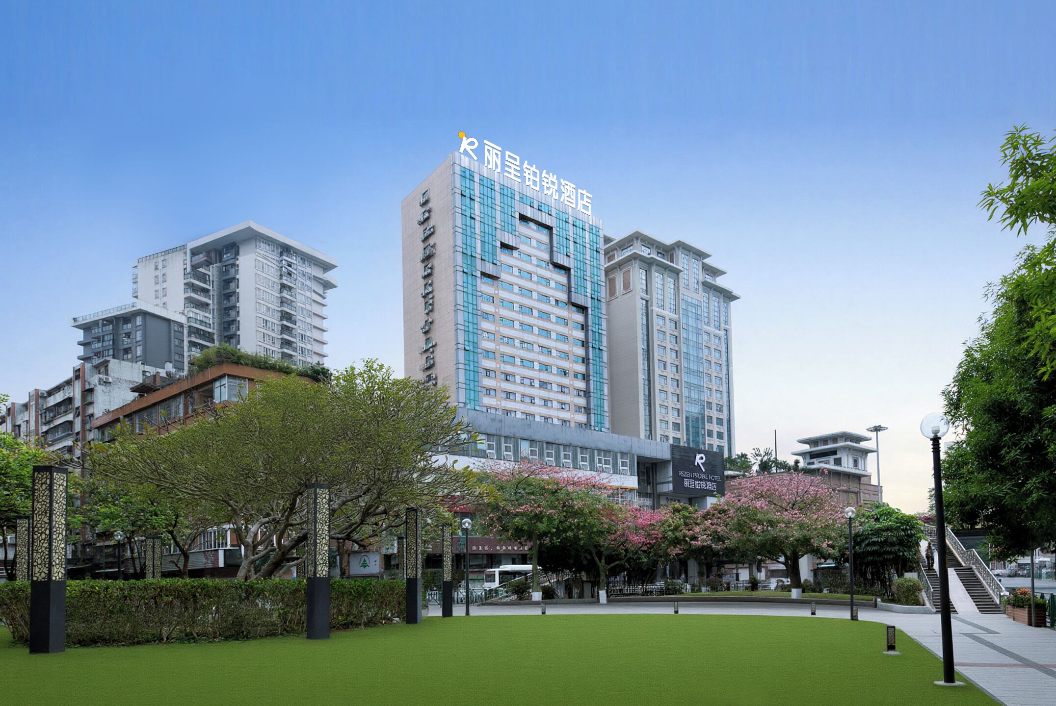 Un hotel moderno con un letrero llamativo, rodeado de vegetación y otros edificios.