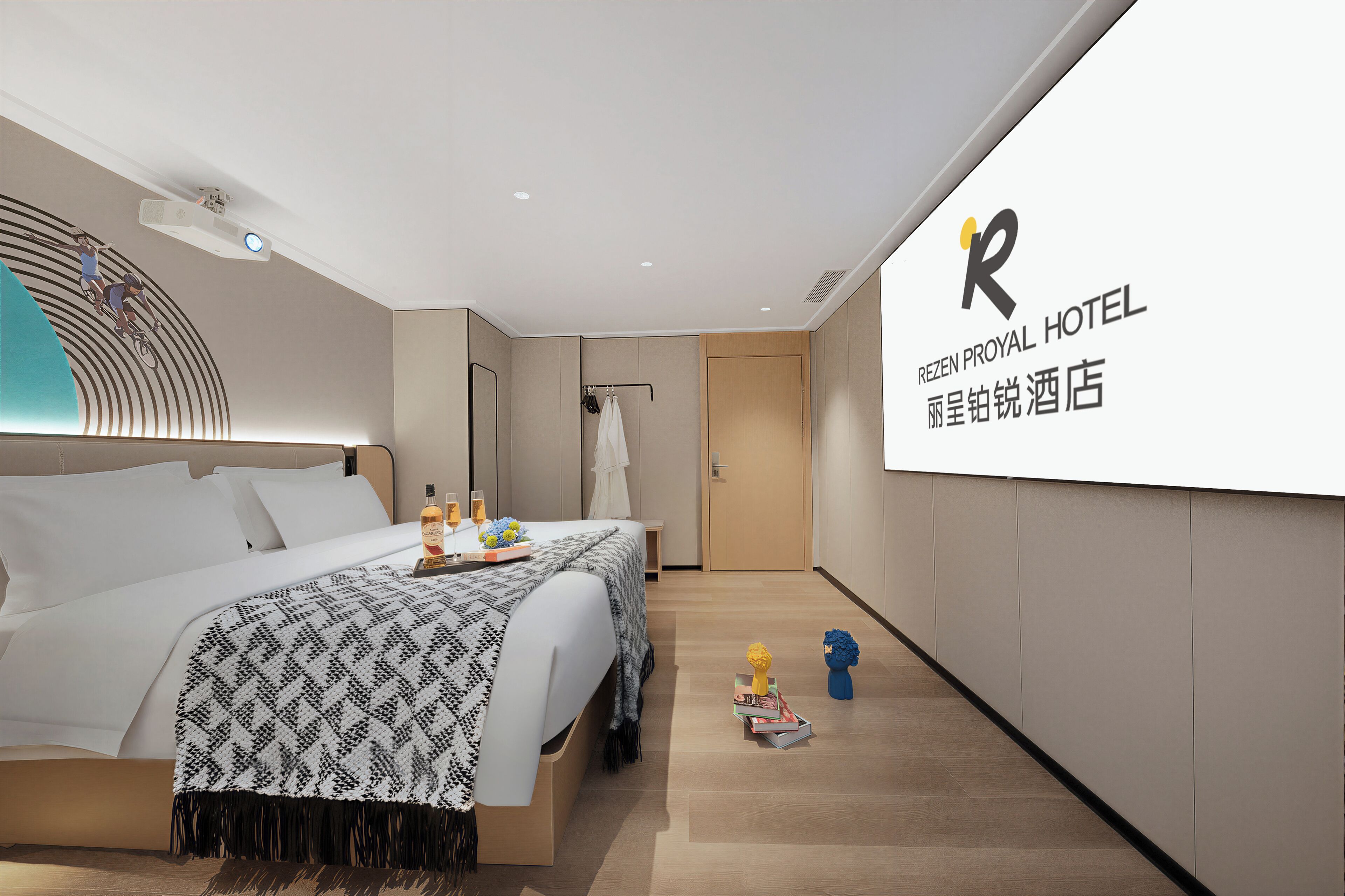 A modern hotel room with a bed, bedside table, and a large screen displaying the hotel name.