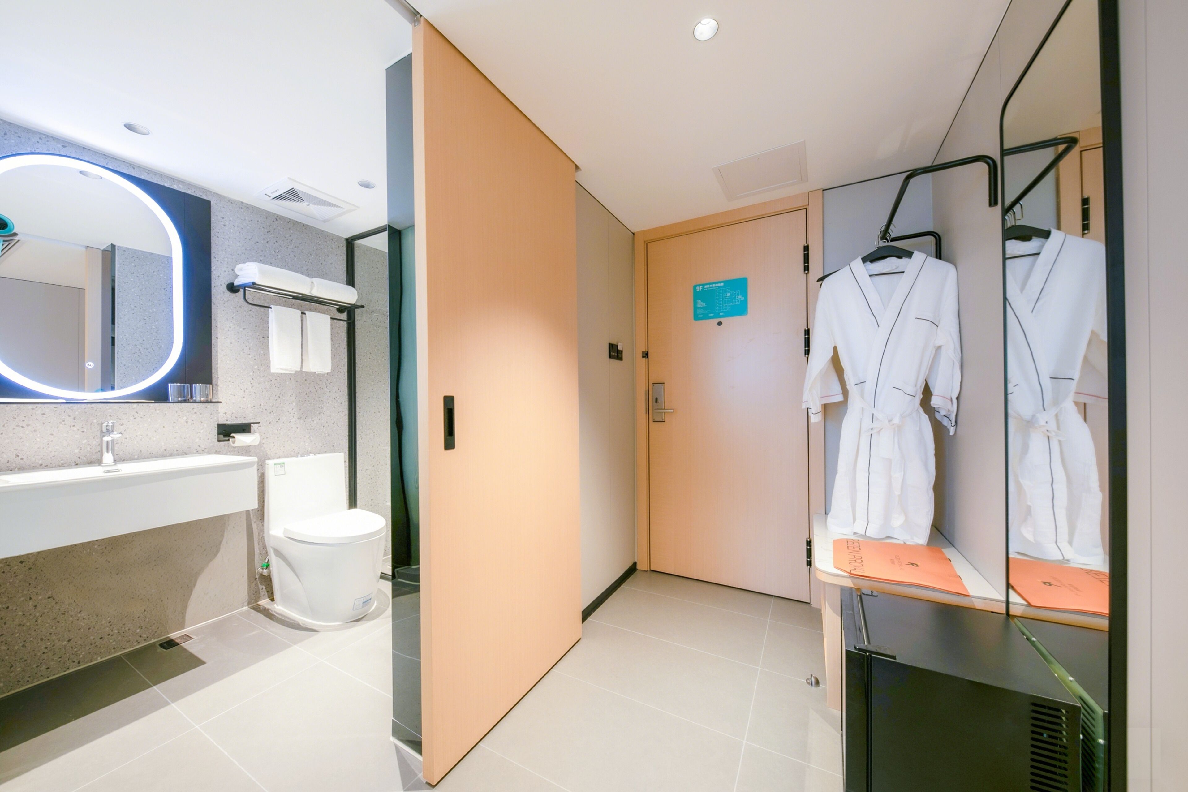 Et moderne badeværelse med spejl, vask, toilet, bøjler til badekåbe og en dør med skilt.