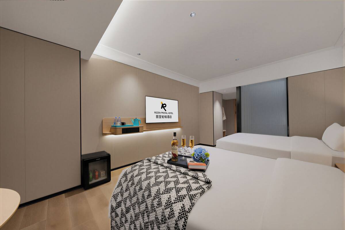 Une chambre d’hôtel moderne, avec un lit, une table de chevet sur laquelle se trouve un plateau de boissons, un tableau encadré au mur et un petit meuble.