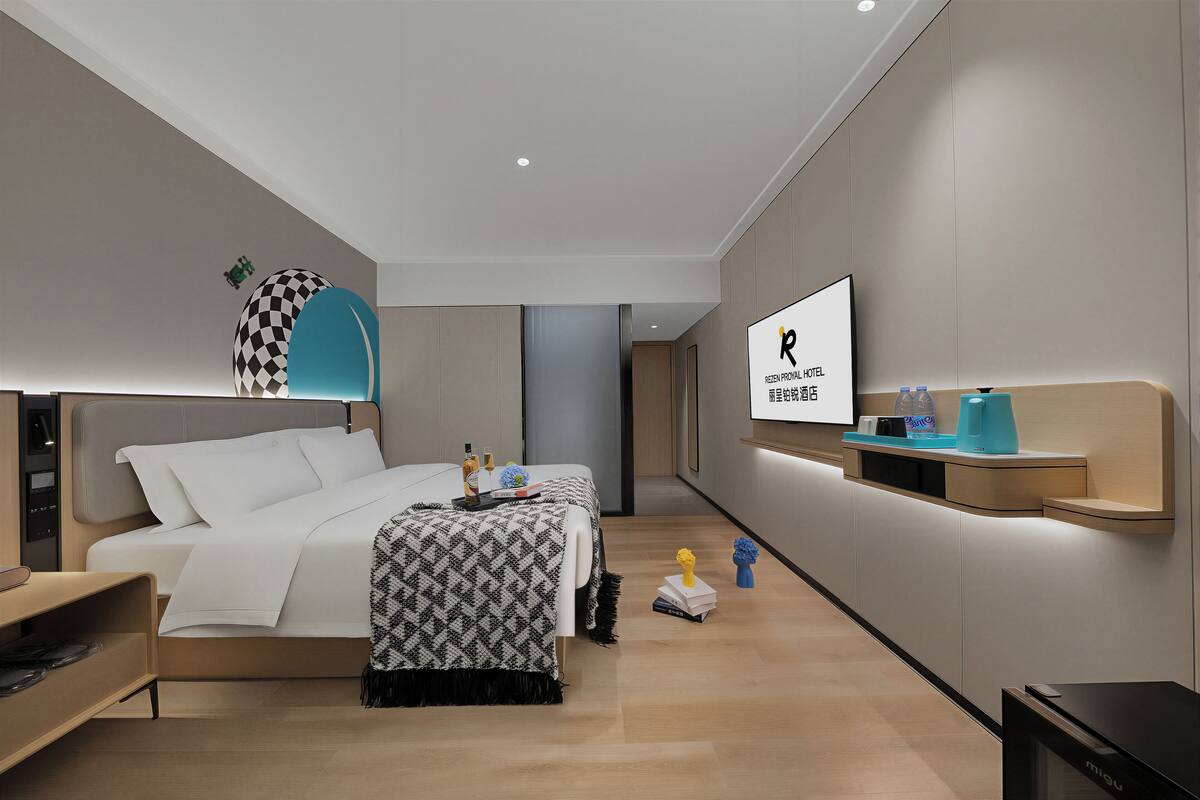 Une chambre d’hôtel moderne équipée d’un lit, d’une table de chevet, d’une télévision et d’une étagère murale où sont disposés divers articles de confort.