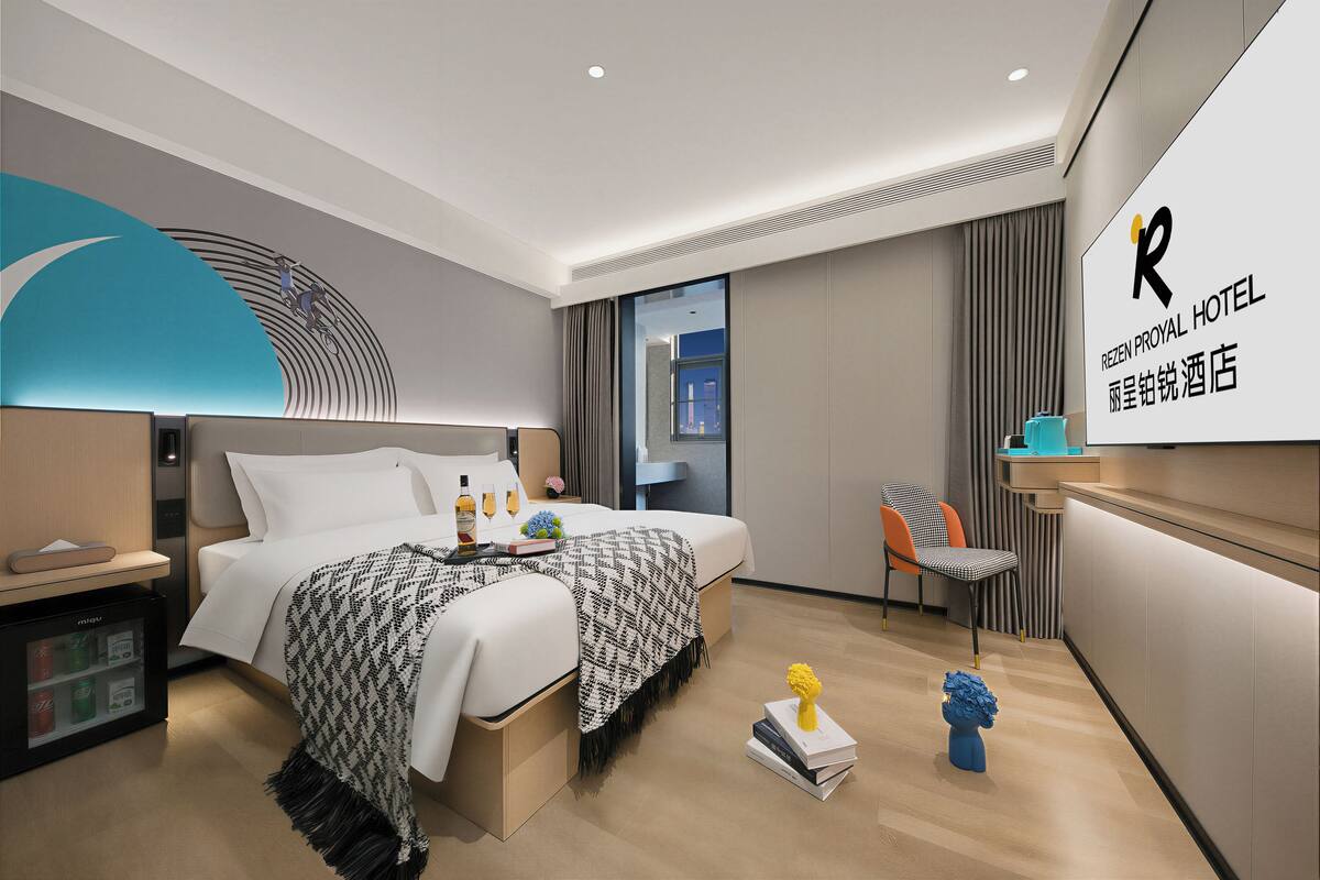 Une chambre d’hôtel moderne équipée d’un lit, d’une table de chevet, d’un minibar et offrant une vue sur la ville.