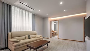 A modern living room with a sofa, coffee table, and a dining area in the background. - Ramada Hotel and Suite Seoul Namdaemun (Seoul)