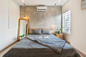 Un dormitorio moderno con una cama gris, cabecera de madera y un espejo grande.